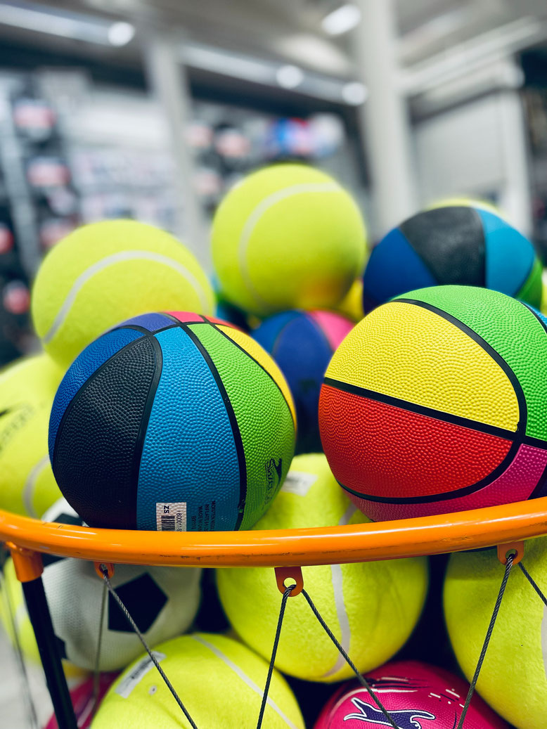 Ein Basketball Korb voller unterschiedlicher, bunter Bälle.